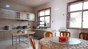 A kitchen with white cabinets, a round glass table, and a window with a view of the street. - Meizhou Island Beach House Resort Hotel (Putian)