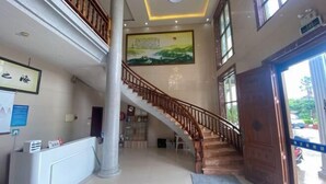 A hotel lobby with a staircase, a reception desk, and a large painting on the wall. - Meizhou Island Beach House Resort Hotel (Putian)
