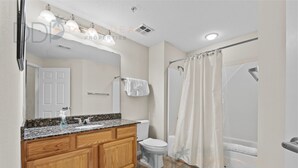 A bathroom with a wooden vanity, a white toilet, a shower with a curtain, and a large mirror.