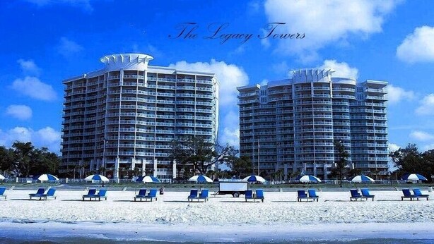 Two high-rise hotels with multiple balconies, a beach with sun umbrellas, and lounge chairs.