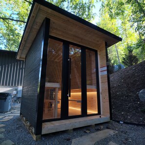 Una pequeña cabaña de madera con puerta de vidrio, un muelle de madera y suelo de grava.