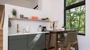 A modern kitchen with a built-in dishwasher, a wooden dining table, and a view of the outdoors through a large window.