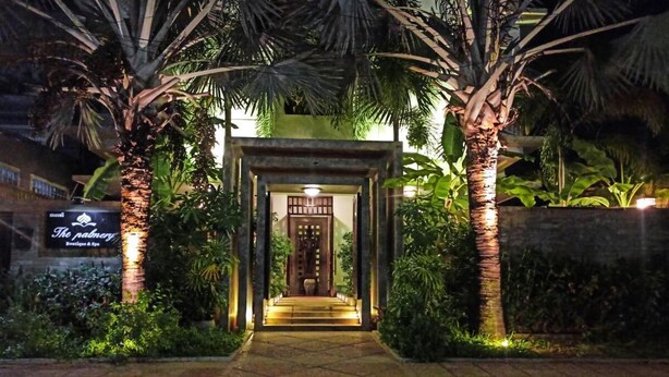 Une entrée bien éclair ée, dotée d’une porte en bois, entourée de palmiers et d’une enseigne indiquant « The Pavilion Boutique & Spa ».