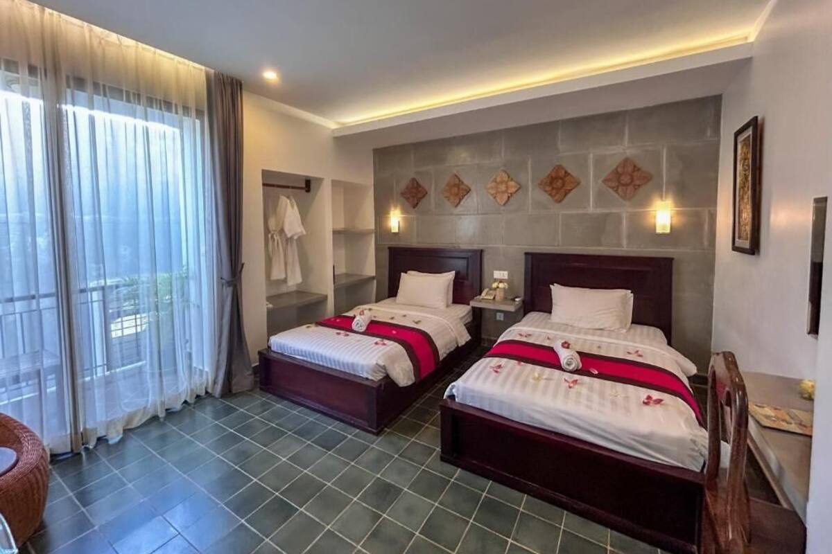 Habitación de hotel con dos camas, un ventanal con cortinas, un televisor de pared y una mesita con una silla.