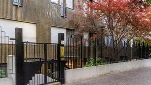 Un bâtiment moderne, doté d’une clôture en métal noir, d’un escalier menant à l’entrée et d’un arbre aux feuilles rouges.