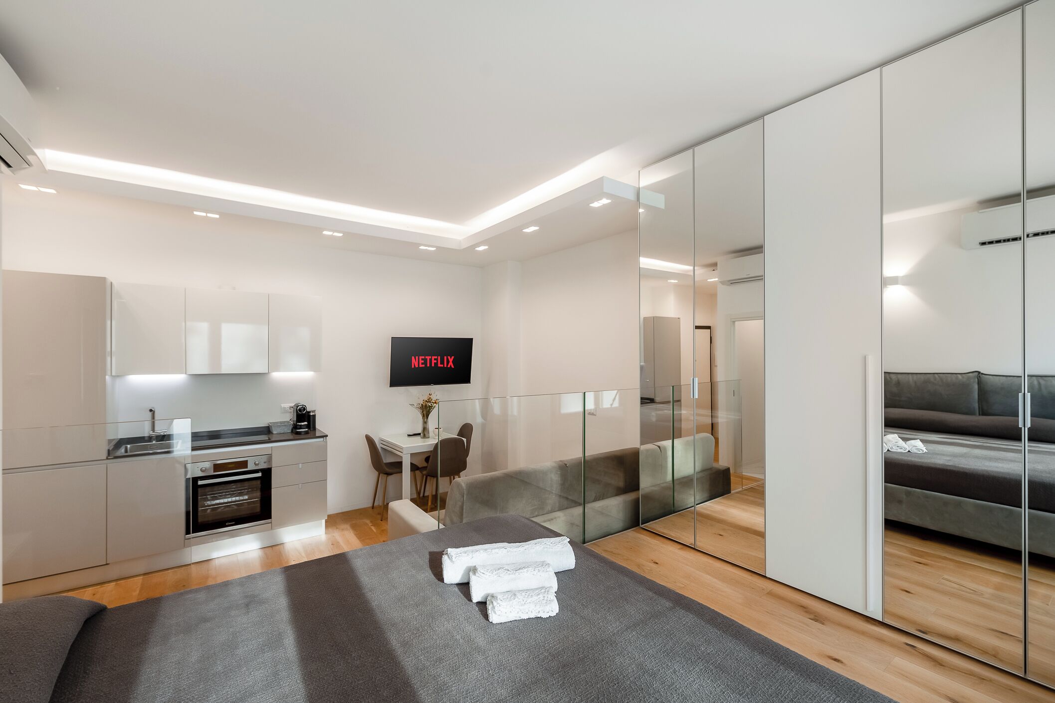 Een moderne hotelkamer met kitchenette, een flatscreen televisie, een bank en een glazen scheidingswand.