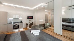 Une chambre d’hôtel moderne dotée d’une kitchenette, d’un téléviseur à écran plat, d’un canapé et d’une cloison en verre.