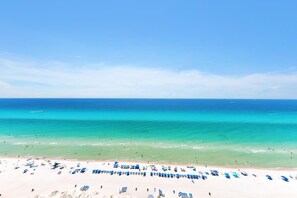 A beach with clear turquoise waters, a sandy shore, and numerous beach umbrellas.