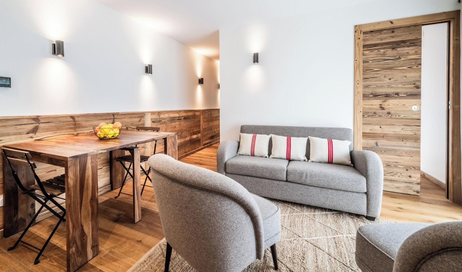 A modern interior with a wooden dining table, grey sofa, and a wooden accent wall.
