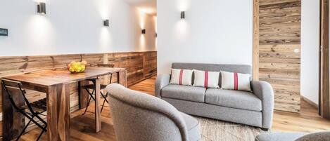 A modern interior with a wooden dining table, grey sofa, and a wooden accent wall.