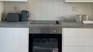 Une cuisine avec des meubles blancs, un dosseret de carreaux disposés en chevron, un four encastré et un grille-pain.