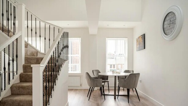 Une pièce spacieuse avec un escalier, un coin repas comprenant une table et des chaises, et une grande fenêtre laissant entrer la lumière naturelle.