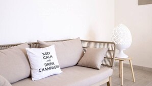 Un canapé beige orné d’un coussin sur lequel est inscrit : « GARDONS NOTRE CALME ET BUVONS DU CHAMPAGNE ».