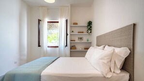 Une chambre à coucher avec un lit, une table de chevet, une fenêtre avec des rideaux et une étagère avec divers objets.