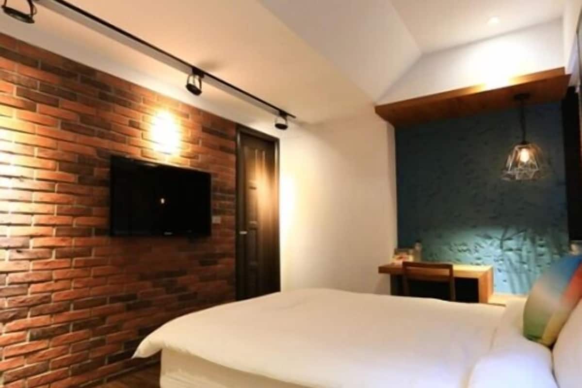 A bedroom with a brick wall, a flat-screen TV mounted above a door, a bed with white bedding, and a hanging light fixture.