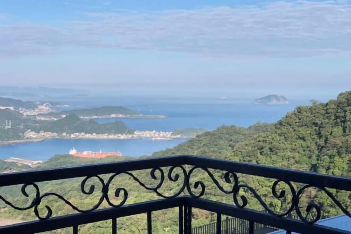 A balcony with a view of a coastal landscape, including hills, a body of water, and a distant island.