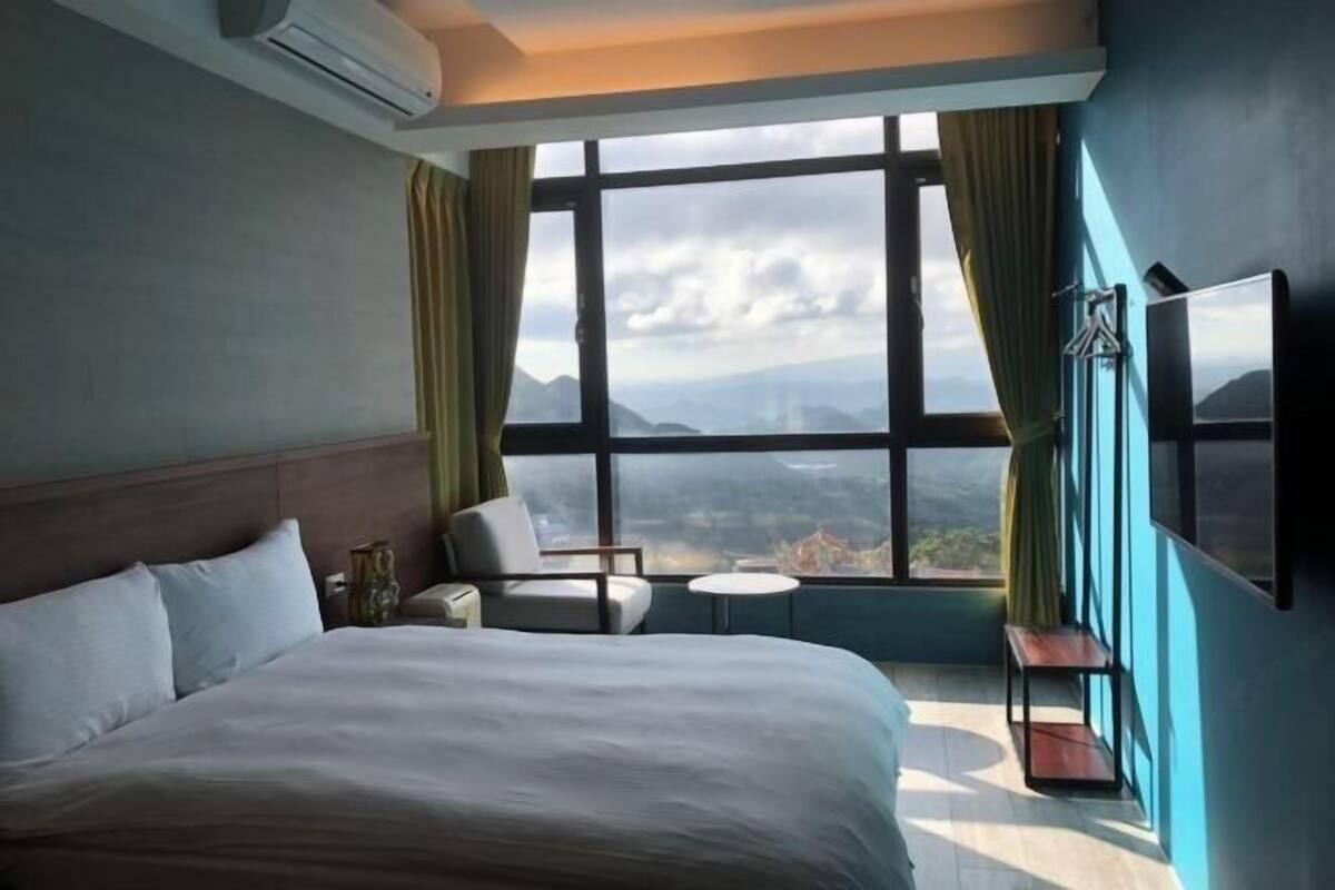 A hotel room with a large bed, a small table, a chair, and a TV mounted on the wall.