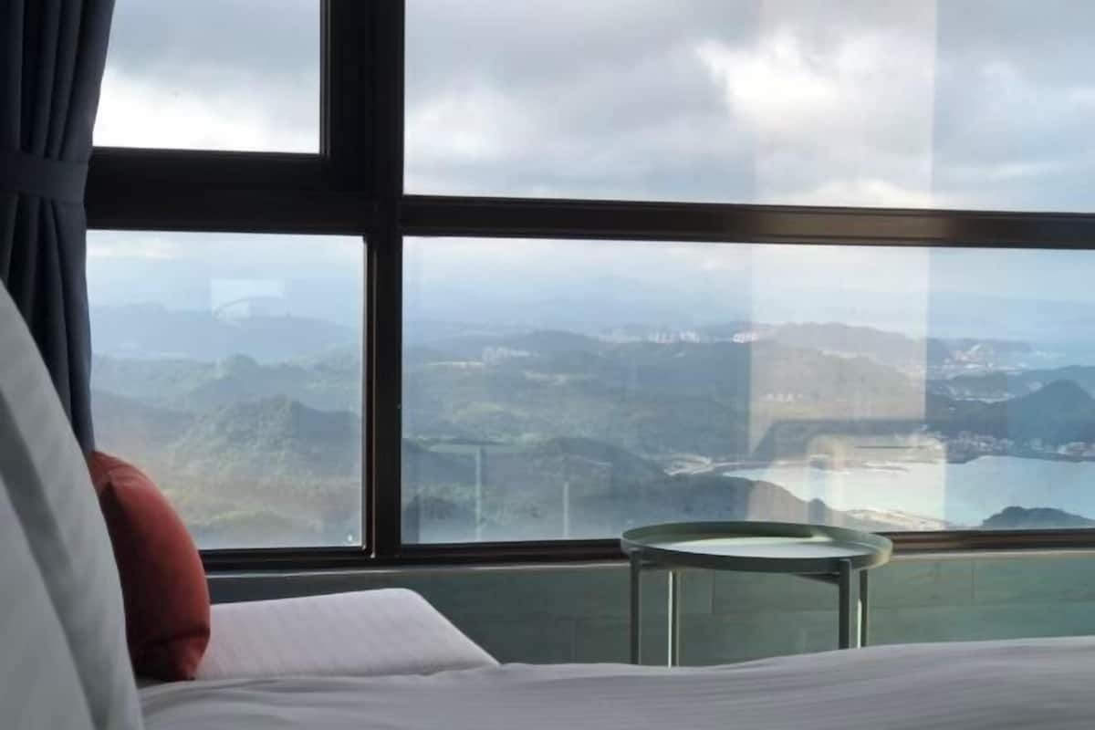 A hotel room with a large window offering a view of a mountainous landscape.