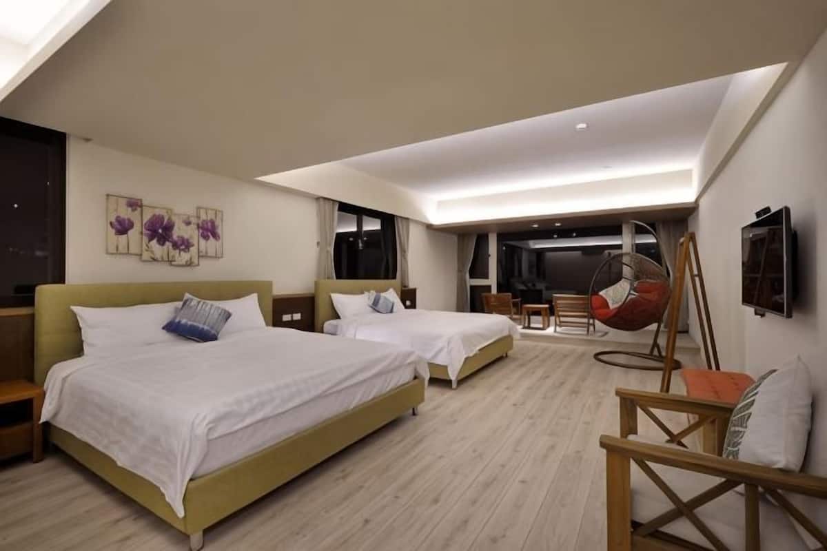 A hotel room with two beds, a hanging chair, a desk, and a large window.