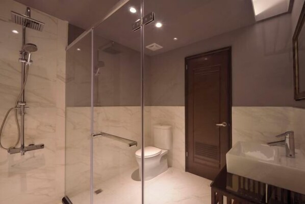 Un baño moderno con ducha envuelta en vidrio, inodoro y lavamanos con espejo arriba.