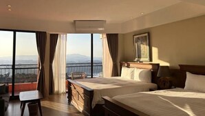 A hotel room with two beds, a desk, and a view of mountains through large windows. - Jiufen Sunshine (New Taipei City)