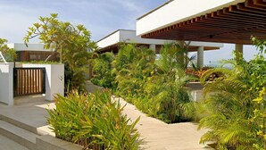 A modern building with a covered outdoor area, surrounded by lush greenery and a pathway leading to a gated entrance. -  Balcón + jacuzzi - 2 habitaciones - Exclusivo - Piscina en la azotea (Cartagena)