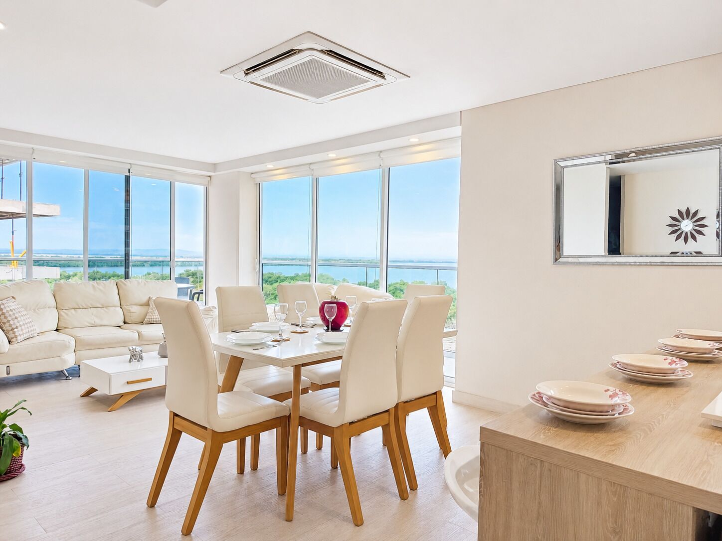 A modern dining area with a view of the sea, a white sofa, and a dining table with chairs.