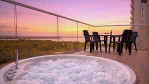 A hot tub with a view of a sunset over a body of water, a table with chairs, and a building in the background. -  Balcón + jacuzzi - 2 habitaciones - Exclusivo - Piscina en la azotea (Cartagena)