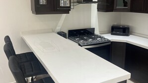 Una cocina moderna con armarios de madera oscura, encimera blanca, estufa a gas, microondas e iluminación colgante.