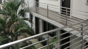 Un edificio residencial de varios pisos con balcones, puertas numeradas y un pequeño jardín con palmeras.