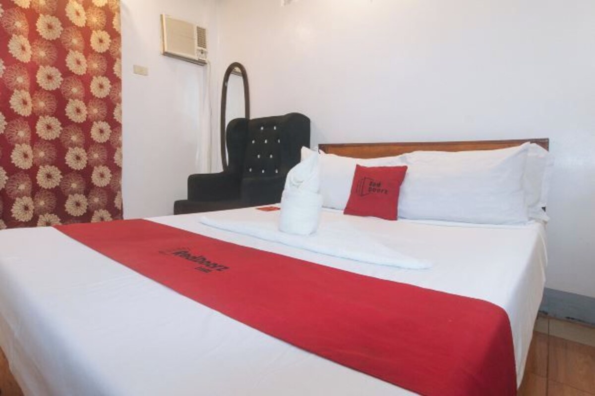 Een hotelkamer met een bed, een rood-witte dekbedovertrek, een zwarte stoel en een rood kussen.