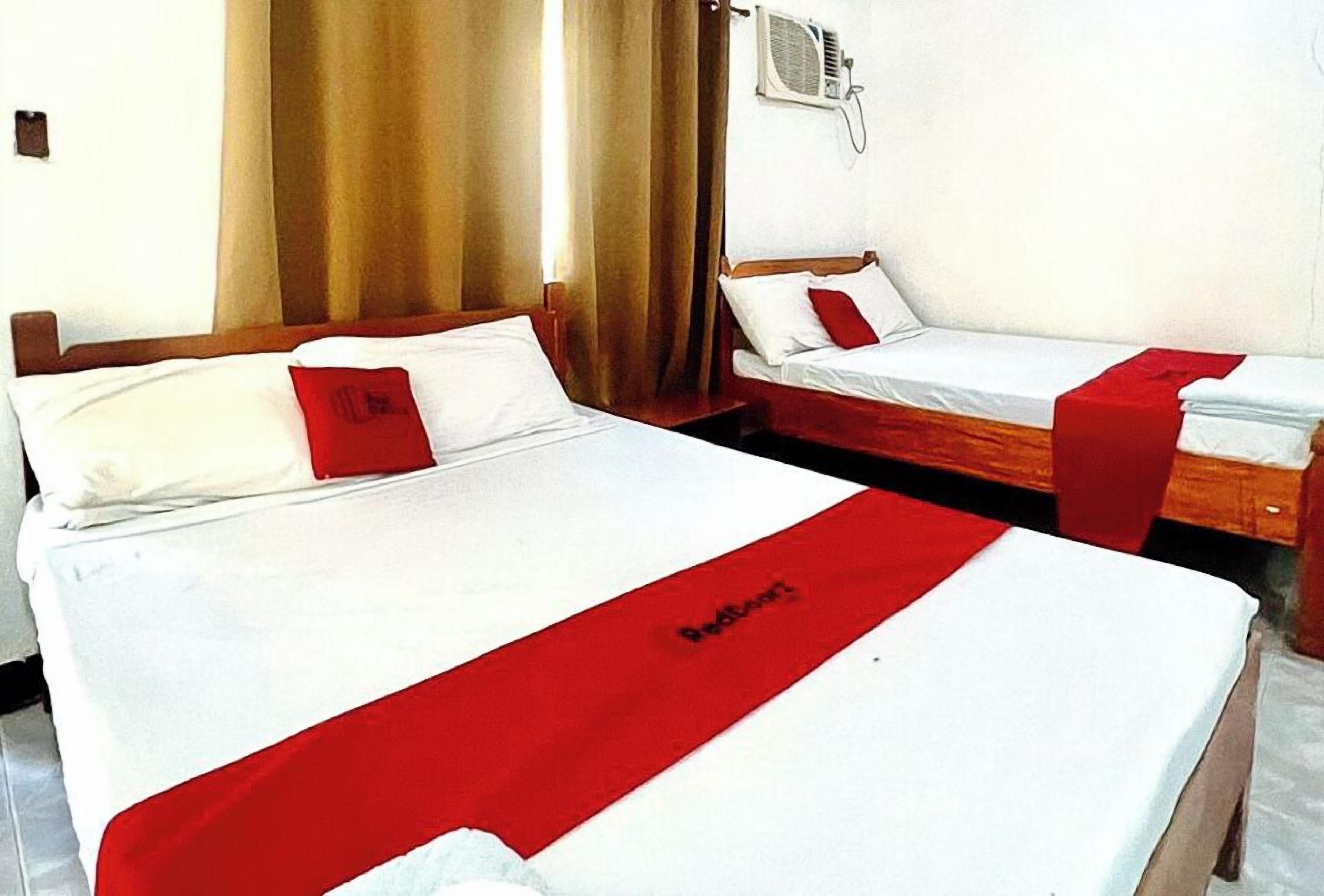 Two single beds with red accents, a wooden headboard, and a wall-mounted air conditioning unit.