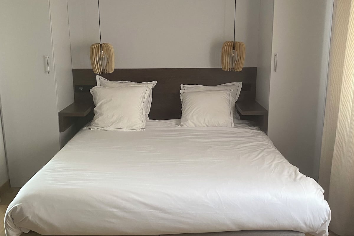 Een moderne slaapkamer met een groot bed, houten vloer en hanglampen.