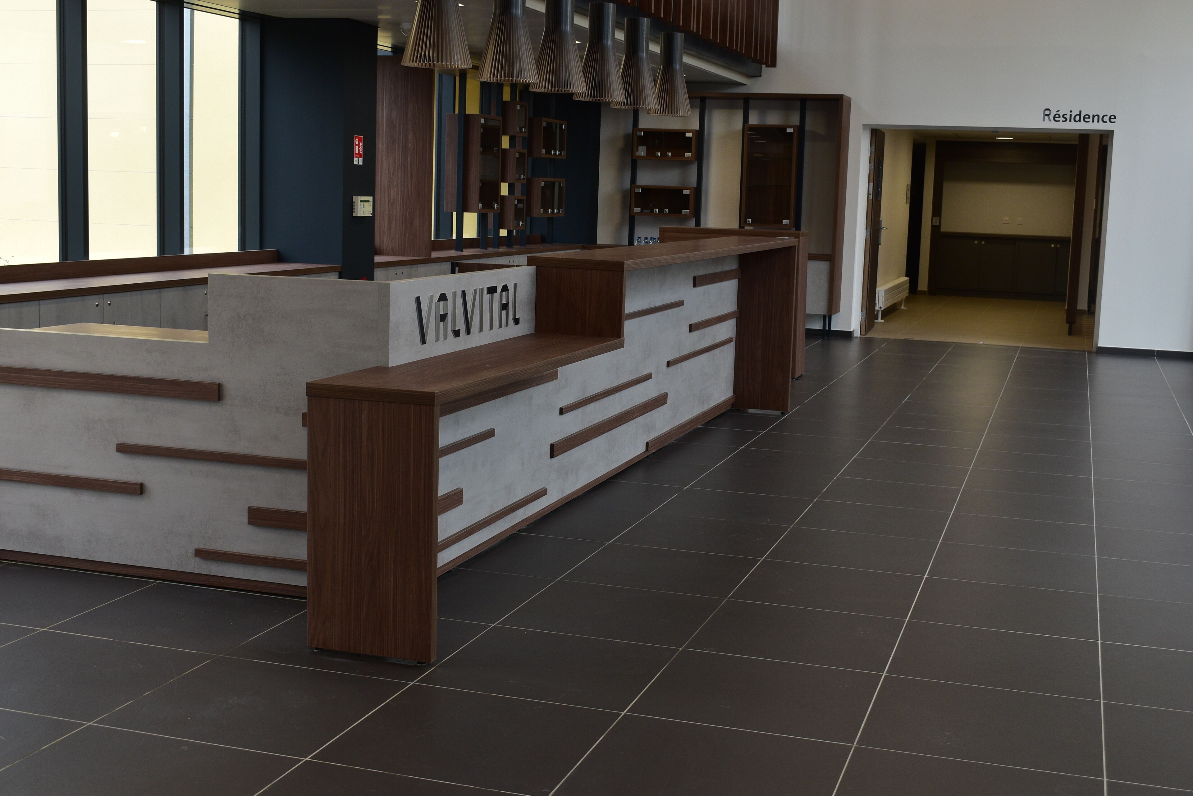 A reception desk with a sign reading "VALVITAL" in a modern lobby with dark tiled floors and wooden accents.