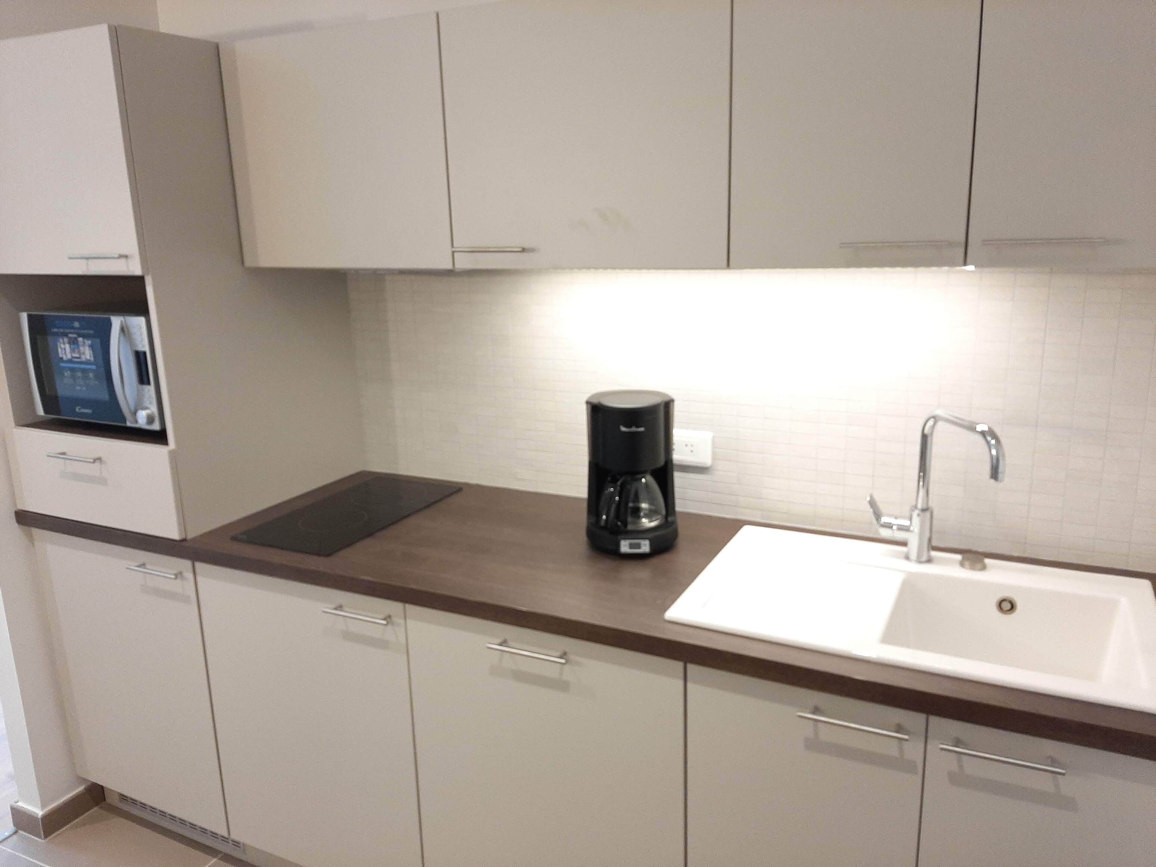 Una cocina moderna con cafetera integrada, un lavamanos y una pantalla digital en la encimera.
