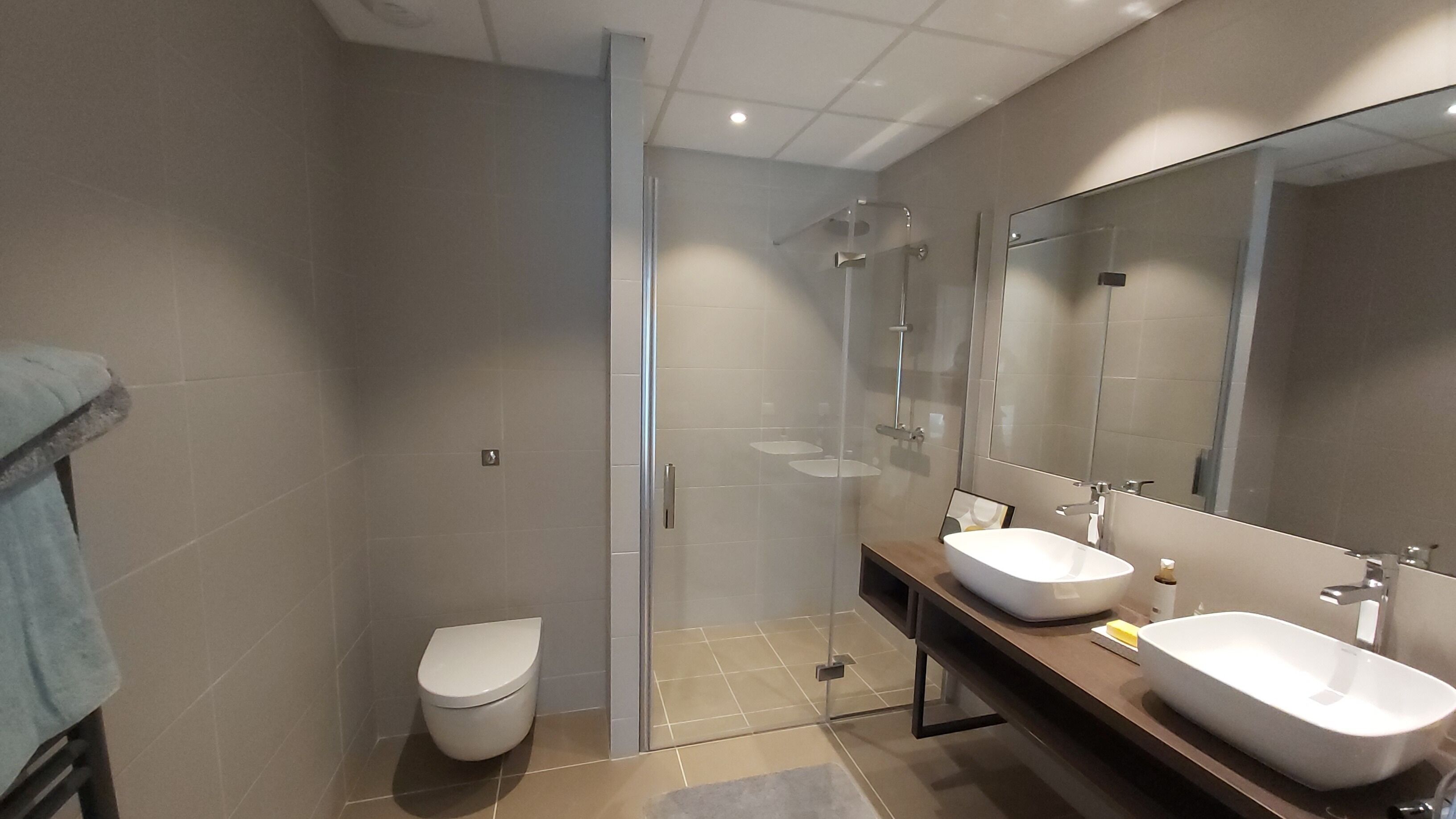 A modern bathroom with a glass-enclosed shower, a toilet, and two sinks with mirrors.