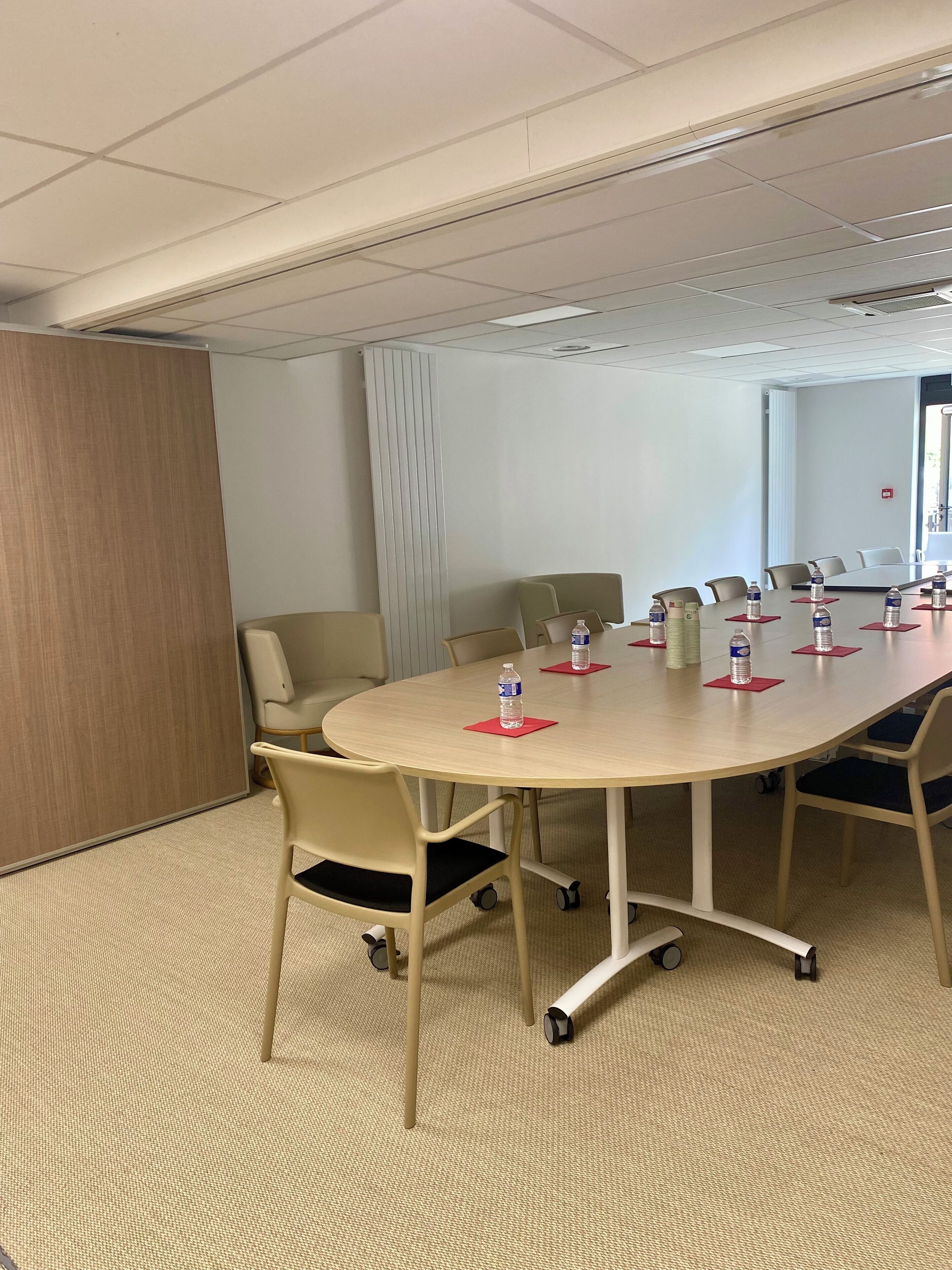 A conference room with a large oval table, several chairs, and water bottles on placemats.