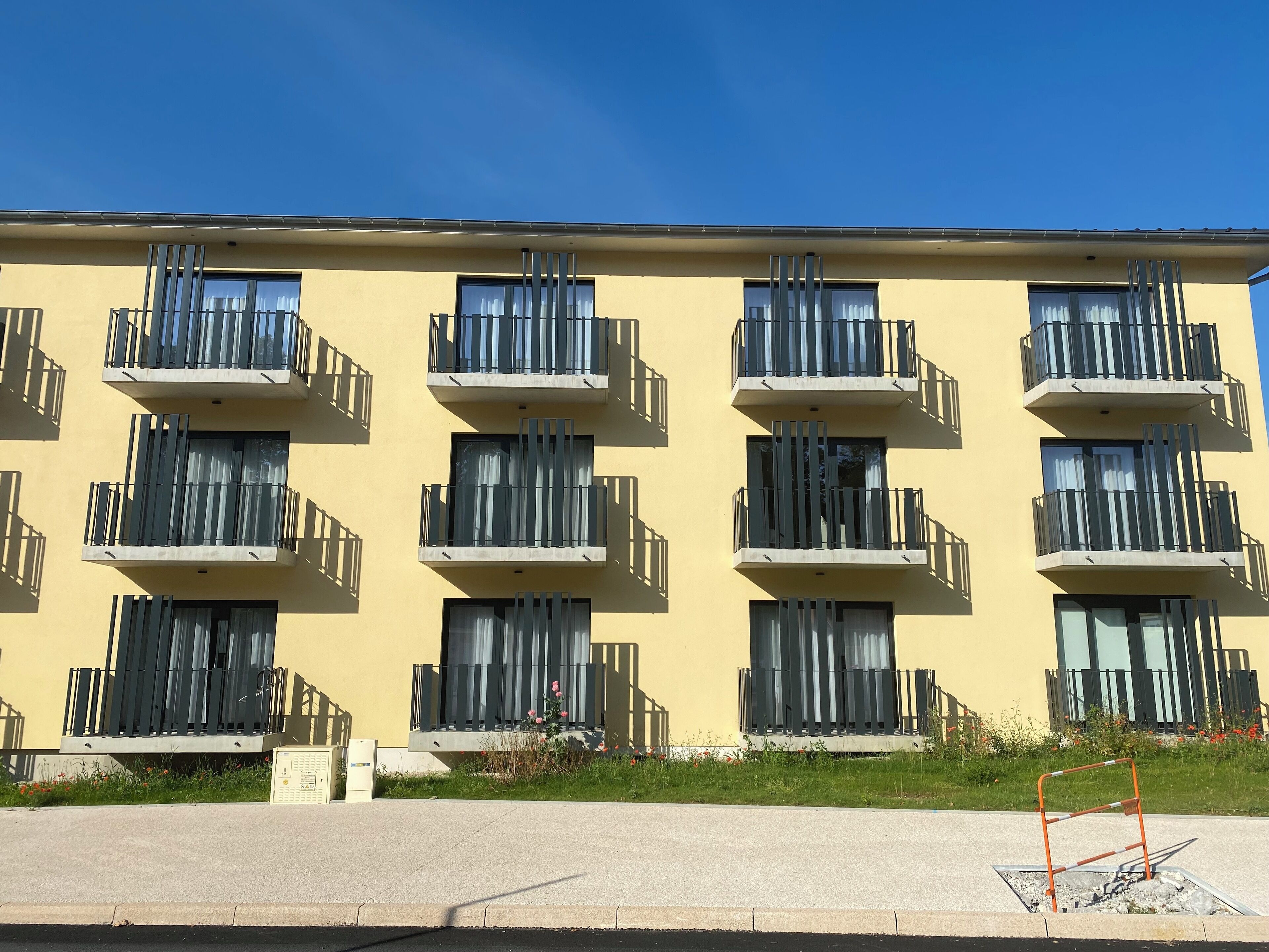 Ein mehrgeschossiges Gebäude mit Balkonen, einer schlichten Fassade und blauem Himmel.