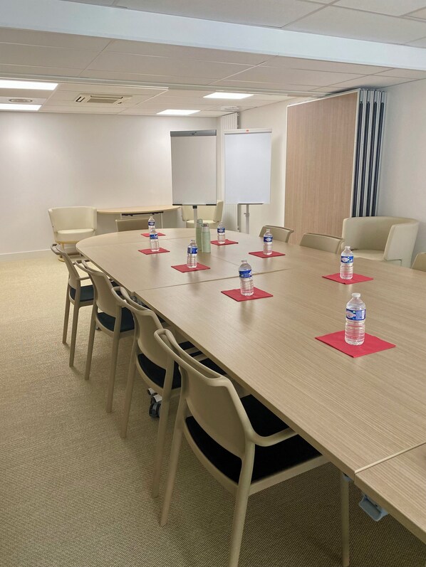 Un salón de conferencias con una larga mesa, sillas, botellas de agua y una pizarra.
