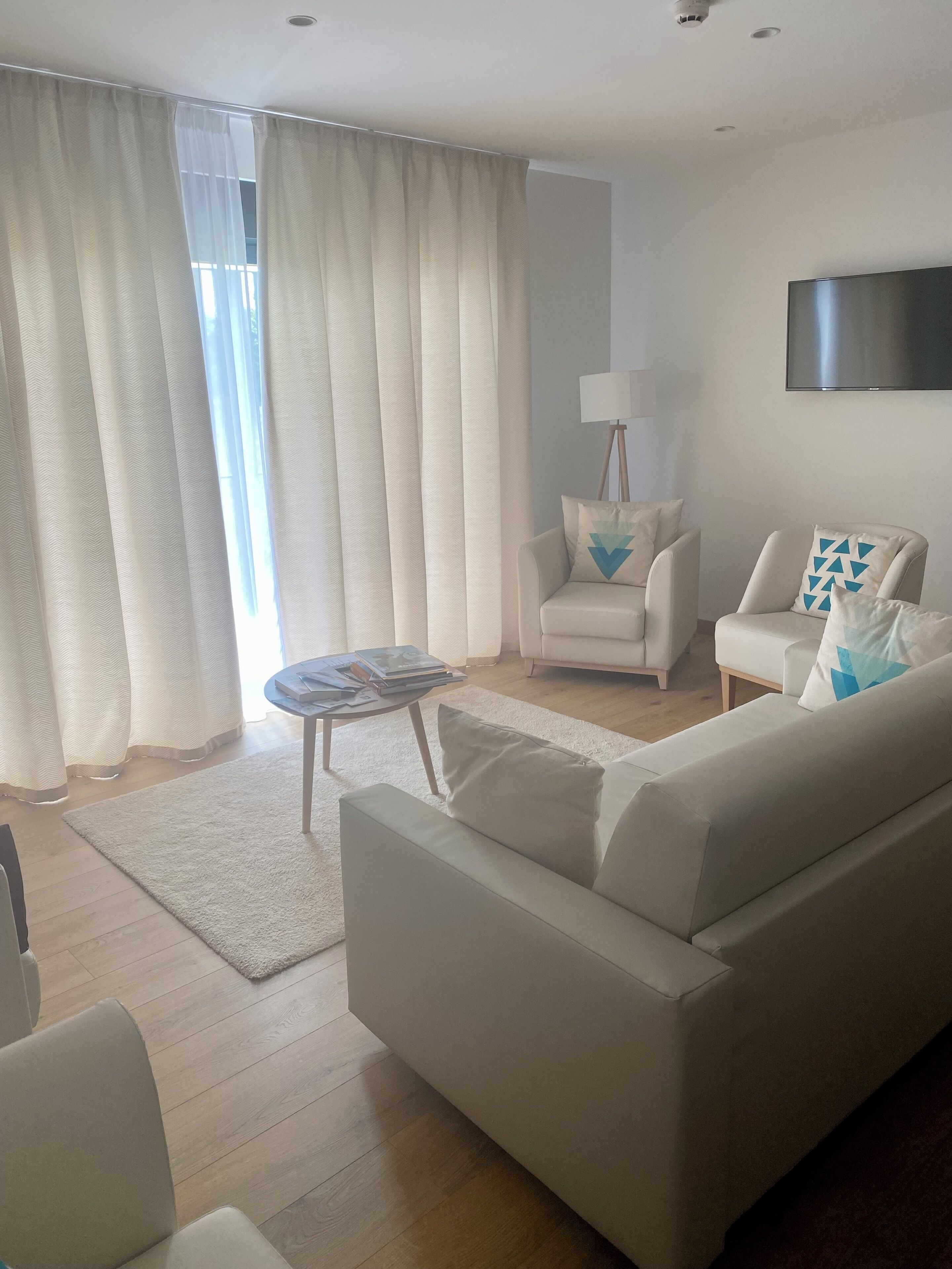 A modern living room with a sofa, armchairs, a coffee table, and a flat-screen TV mounted on the wall.