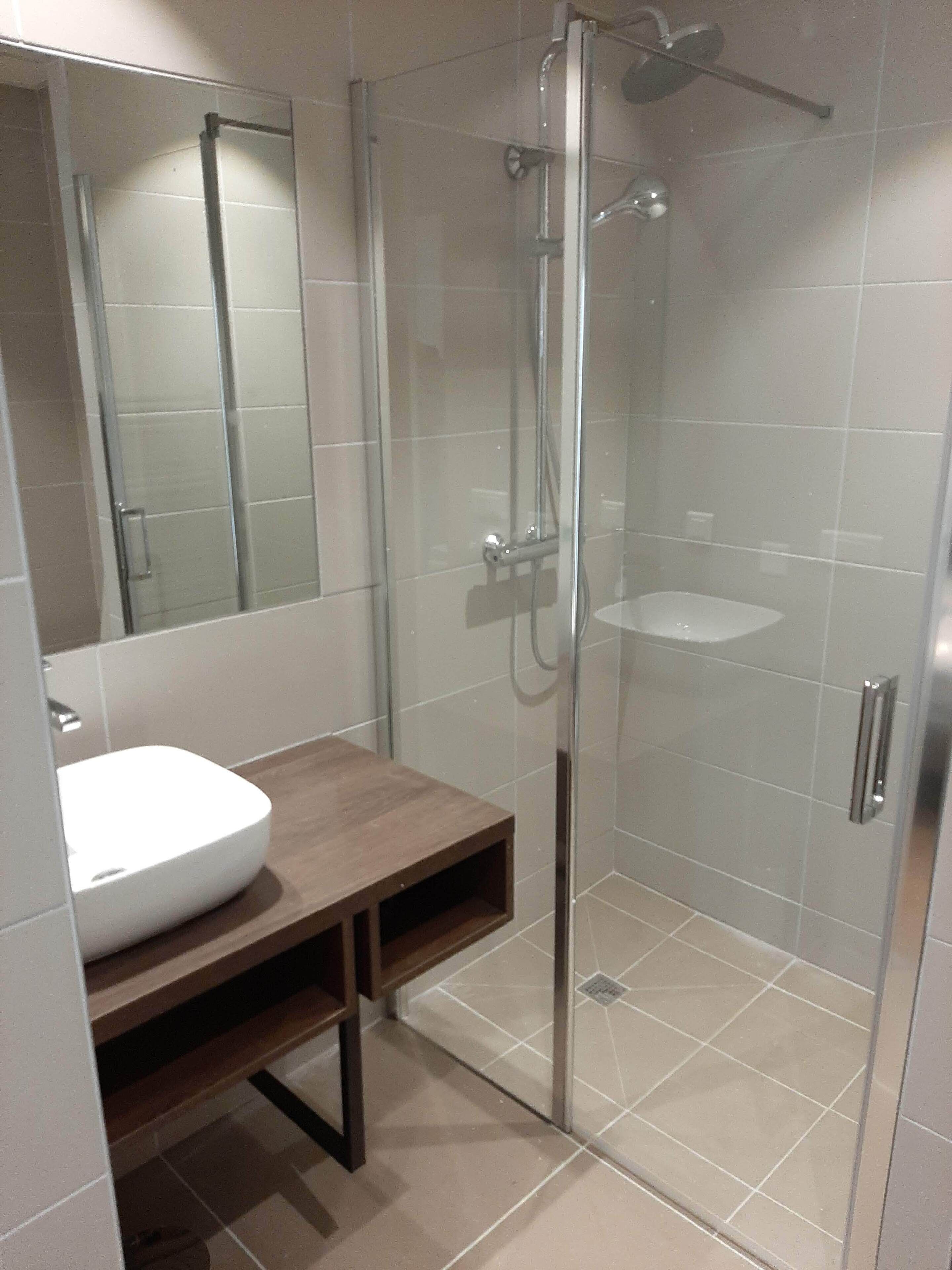 Une salle de bain moderne avec une douche à parois de verre, un lavabo blanc et un meuble-lavabo en bois.