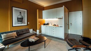 Een moderne woonkamer met een bank, een salontafel en een zwarte stoel. Er is een keuken met witte kastjes en een aanrecht.