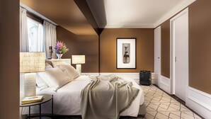 Een hotelkamer met een bed, bedlampjes, een klein tafeltje met boeken, een lijst met foto aan de muur, en een koffer op de vloer.