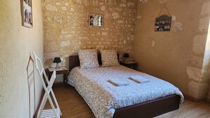 Une chambre avec un mur en pierre, un lit avec une literie à motifs, deux tables de chevet avec des lampes et une échelle en bois.