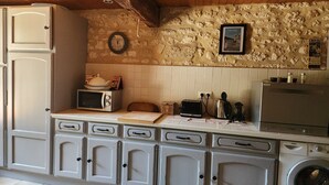 Une cuisine avec un mur en pierre, une horloge, un tableau encadré, un four à micro-ondes, un grille-pain, une bouilloire et un lave-linge.