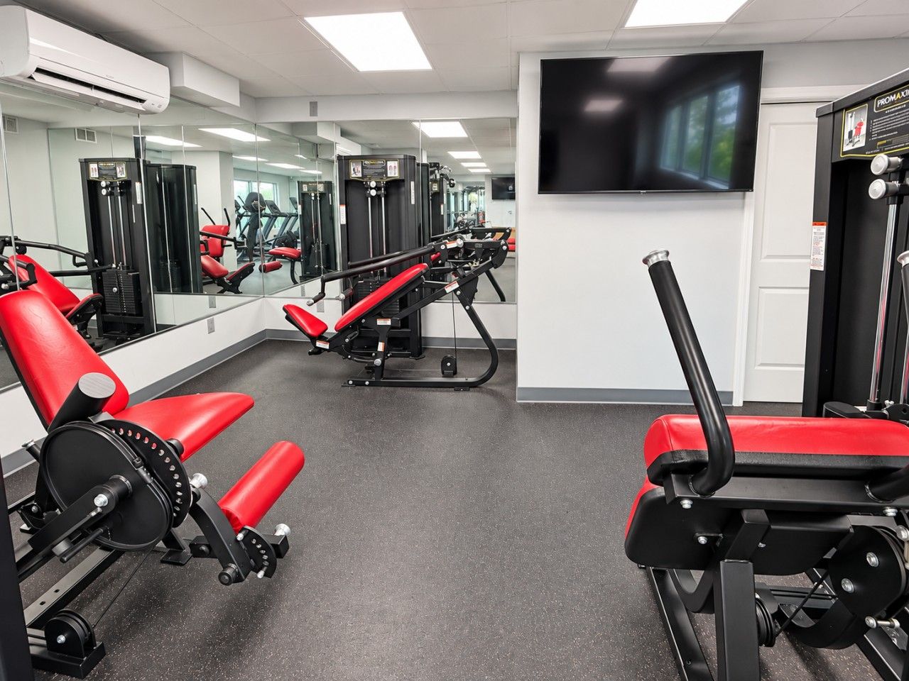 Ein Fitnessraum mit Trainingsgeräten, einem großen Spiegel und einem Fernseher an der Wand.