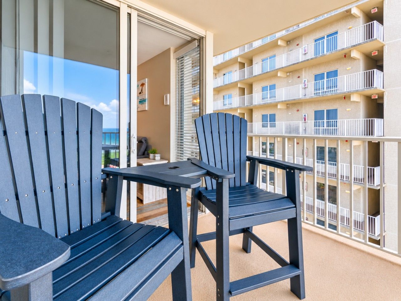 Een balkon met twee stoelen en een tafeltje, met uitzicht op een gebouw met meerdere balkons.
