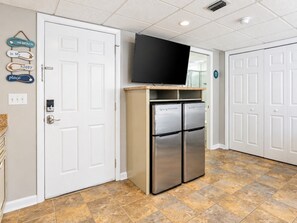 Una cocina con un refrigerador de acero inoxidable, un televisor de pantalla plana montado encima y piso de baldosas.