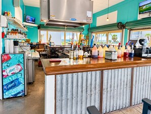 A bar area with a counter, shelves with bottles, a television, and a view of the outdoors.