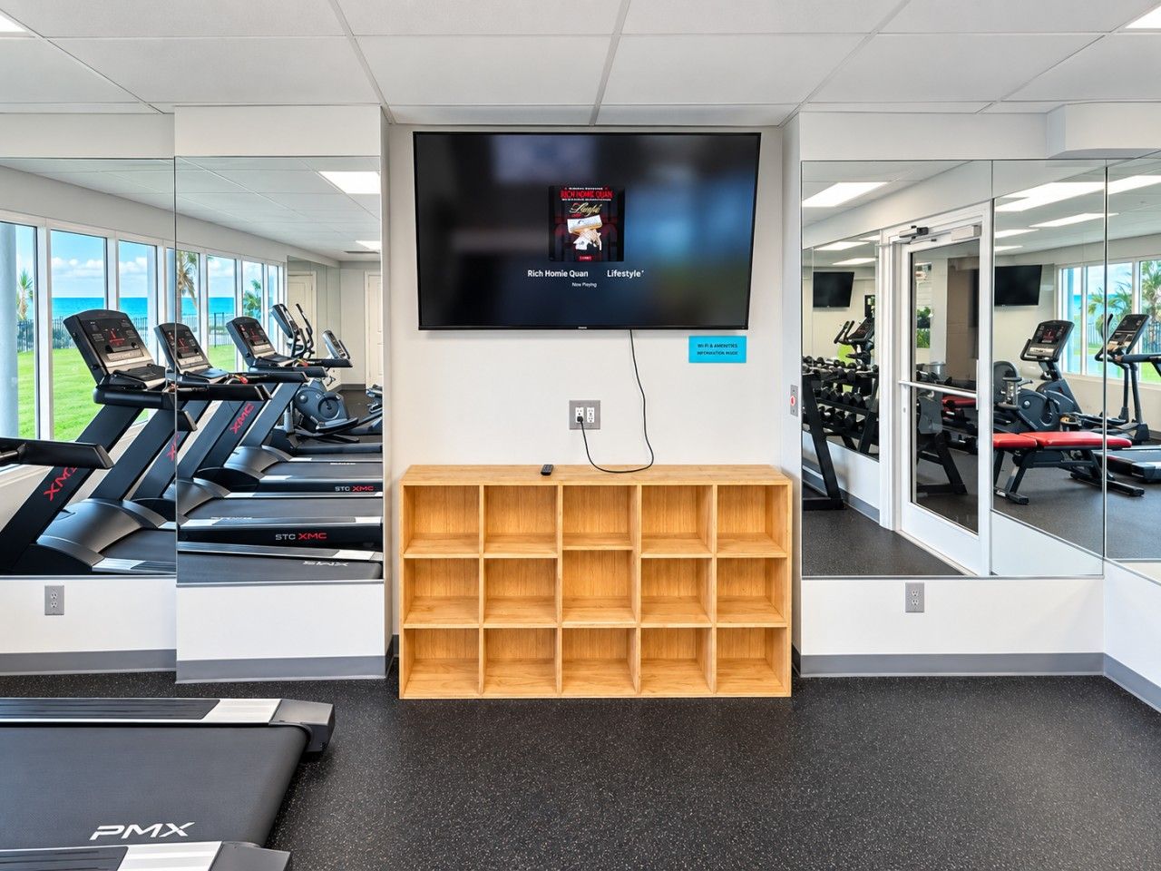 A gym with treadmills, a TV screen, and a wooden shelf unit.